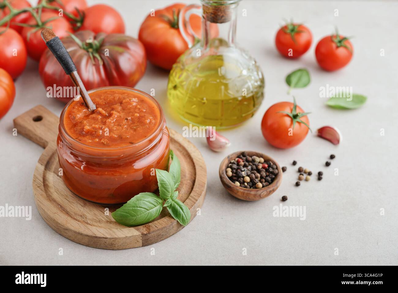 Traditional tomato sauce in a glass jar with fresh basil, ripe tomatoes, garlic and pepper on wooden cutting board, closeup Stock Photo