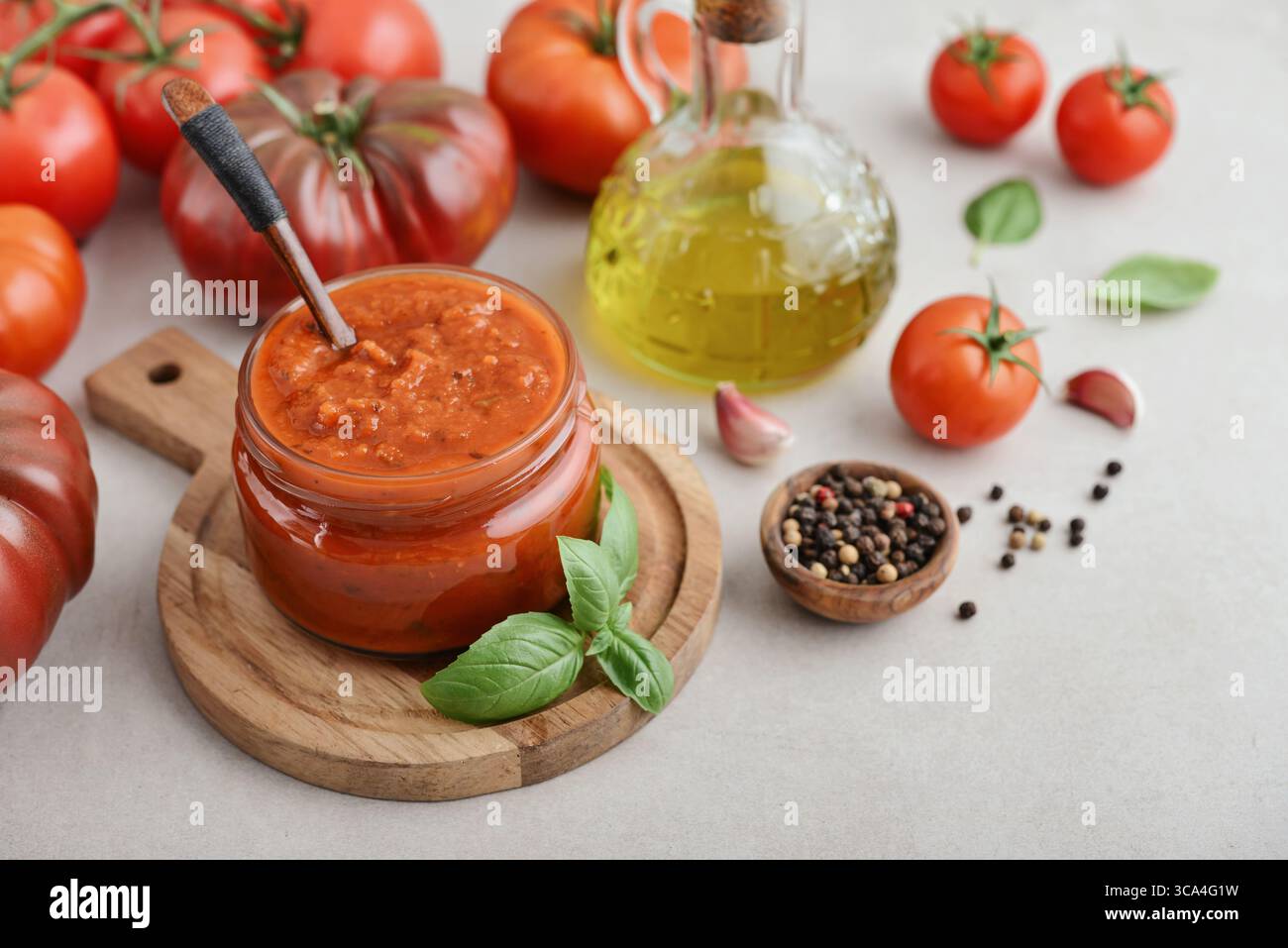 Traditional tomato sauce in a glass jar with fresh basil, ripe tomatoes, garlic and pepper on wooden cutting board, closeup Stock Photo