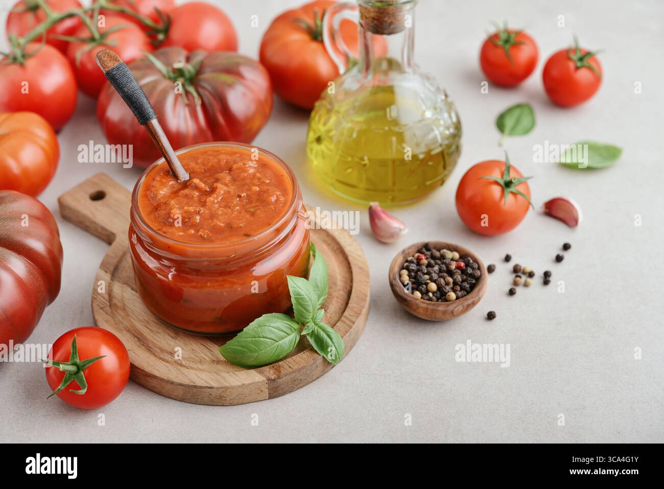 Traditional tomato sauce in a glass jar with fresh basil, ripe tomatoes, garlic and pepper on wooden cutting board, closeup Stock Photo
