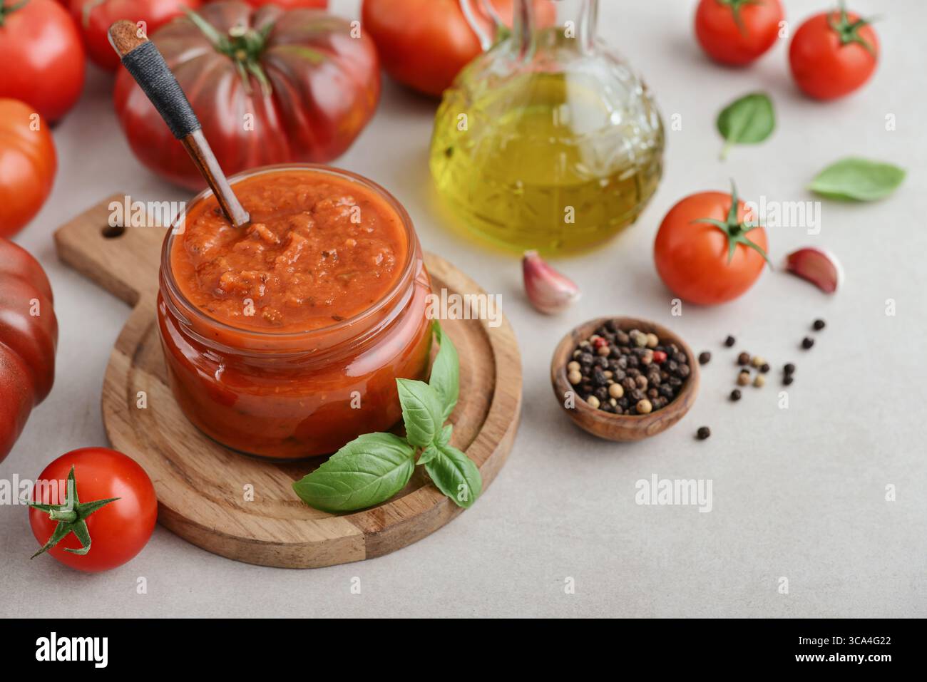 Traditional tomato sauce in a glass jar with fresh basil, ripe tomatoes, garlic and pepper on wooden cutting board, closeup Stock Photo