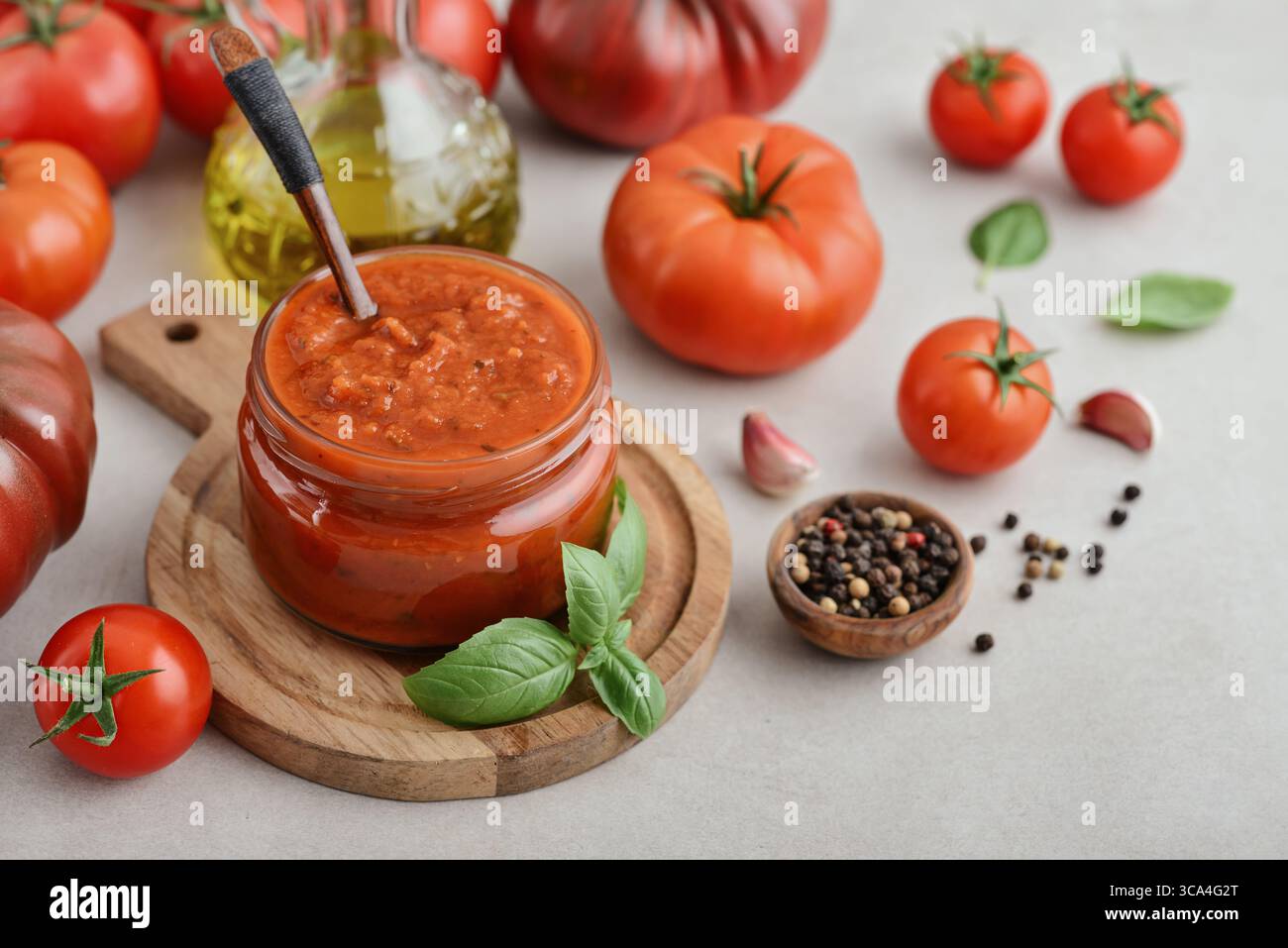 Traditional tomato sauce in a glass jar with fresh basil, ripe tomatoes, garlic and pepper on wooden cutting board, closeup Stock Photo
