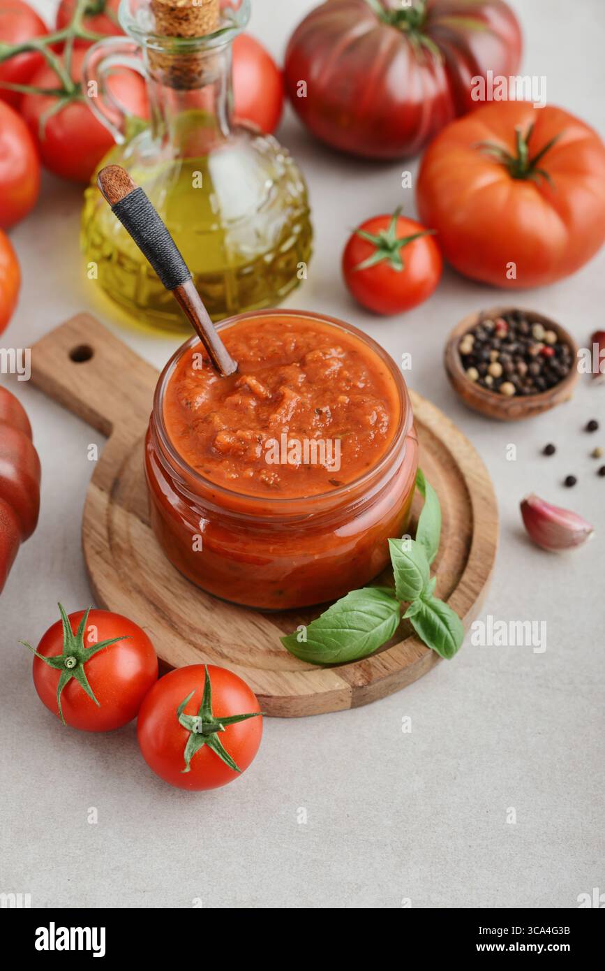 Traditional tomato sauce in a glass jar with fresh basil, ripe tomatoes, garlic and pepper on wooden cutting board, closeup Stock Photo