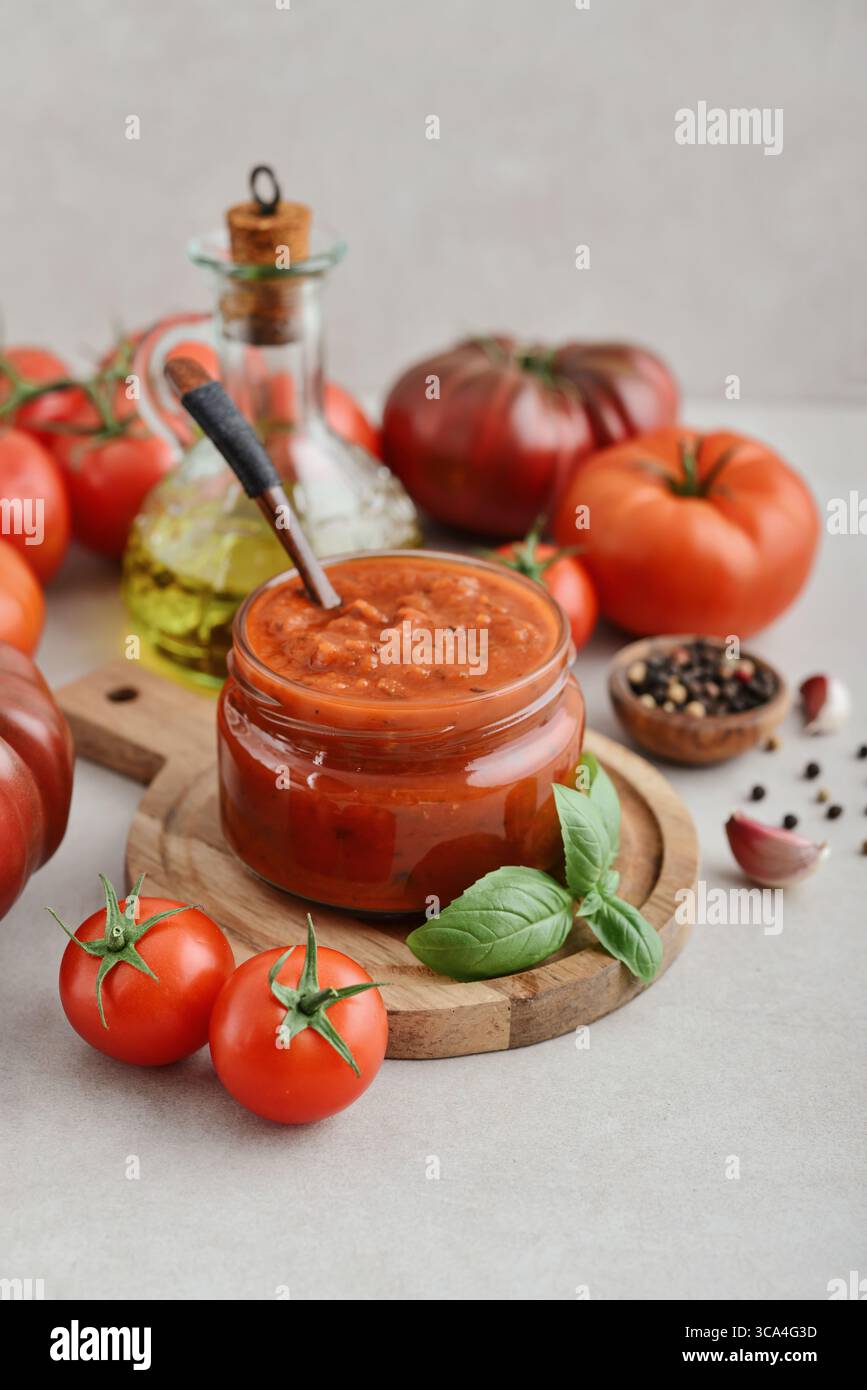 Traditional tomato sauce in a glass jar with fresh basil, ripe tomatoes, garlic and pepper on wooden cutting board, closeup Stock Photo