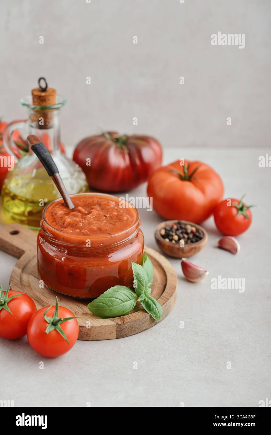 Traditional tomato sauce in a glass jar with fresh basil, ripe tomatoes, garlic and pepper on wooden cutting board, closeup Stock Photo