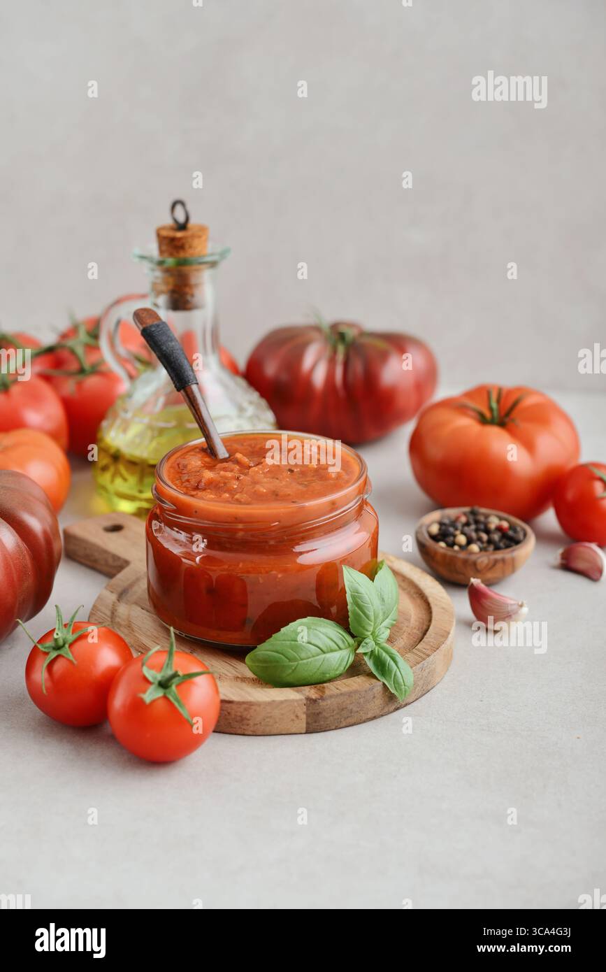 Traditional tomato sauce in a glass jar with fresh basil, ripe tomatoes, garlic and pepper on wooden cutting board, closeup Stock Photo