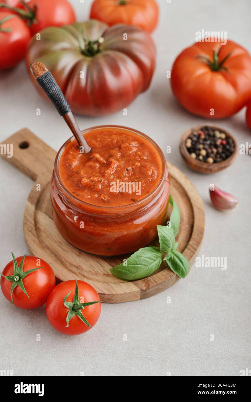 Traditional tomato sauce in a glass jar with fresh basil, ripe tomatoes, garlic and pepper on wooden cutting board, closeup Stock Photo