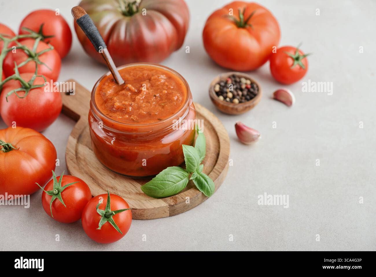 Traditional tomato sauce in a glass jar with fresh basil, ripe tomatoes, garlic and pepper on wooden cutting board, closeup Stock Photo