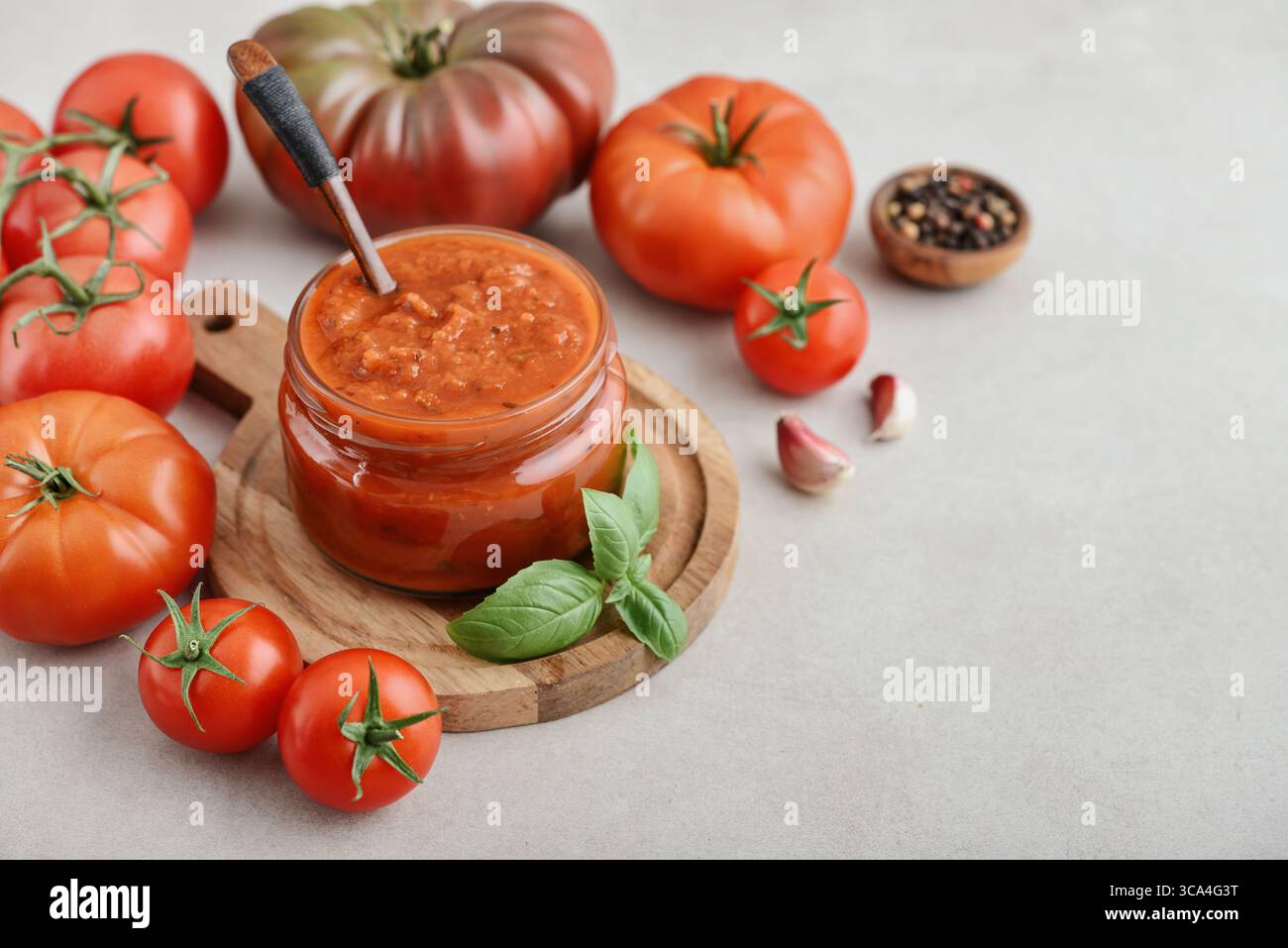 Traditional tomato sauce in a glass jar with fresh basil, ripe tomatoes, garlic and pepper on wooden cutting board, closeup Stock Photo