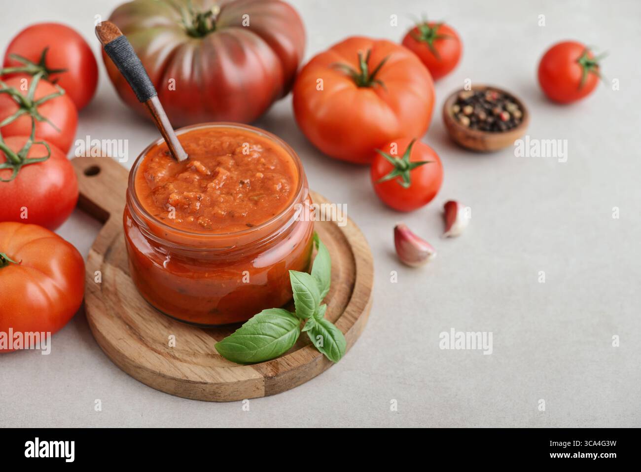 Traditional tomato sauce in a glass jar with fresh basil, ripe tomatoes, garlic and pepper on wooden cutting board, closeup Stock Photo