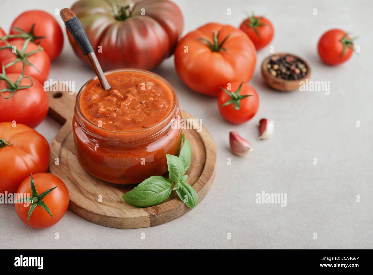 Traditional tomato sauce in a glass jar with fresh basil, ripe tomatoes, garlic and pepper on wooden cutting board, closeup Stock Photo