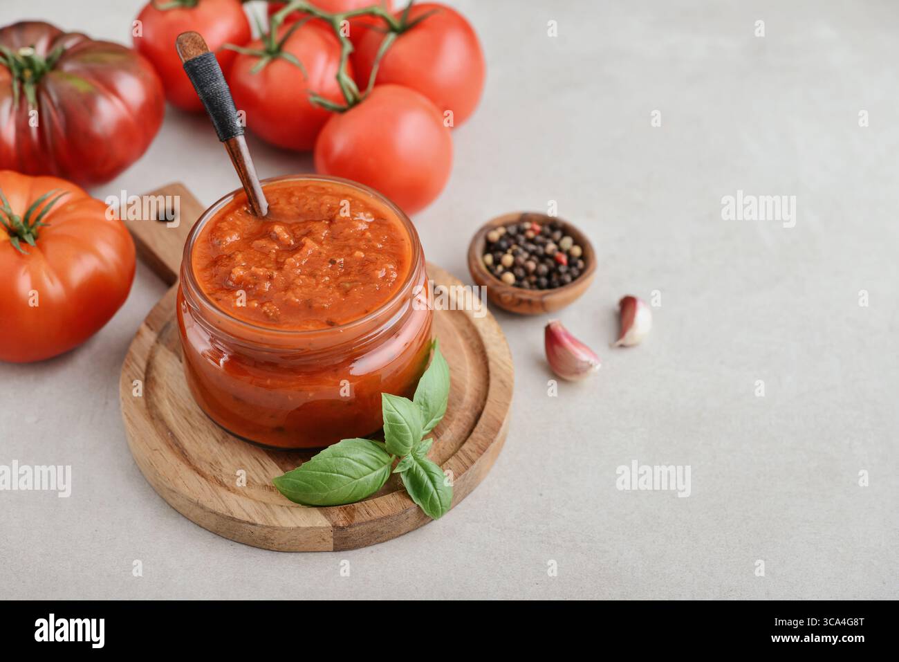 Traditional tomato sauce in a glass jar with fresh basil, ripe tomatoes, garlic and pepper on wooden cutting board, closeup Stock Photo