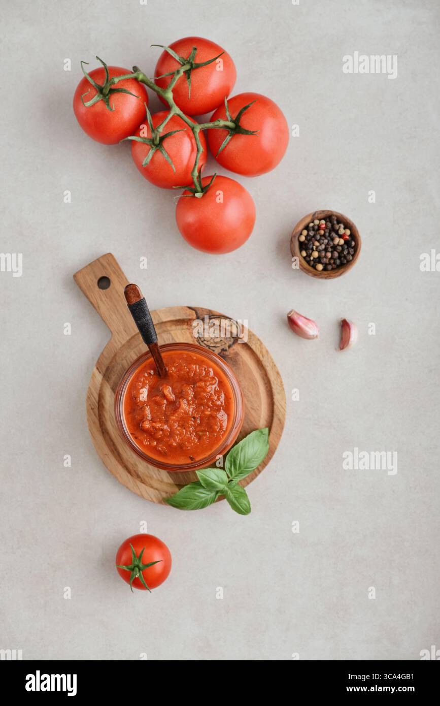 Traditional tomato sauce in a glass jar with fresh basil, ripe tomatoes, garlic and pepper on wooden cutting board, top view Stock Photo
