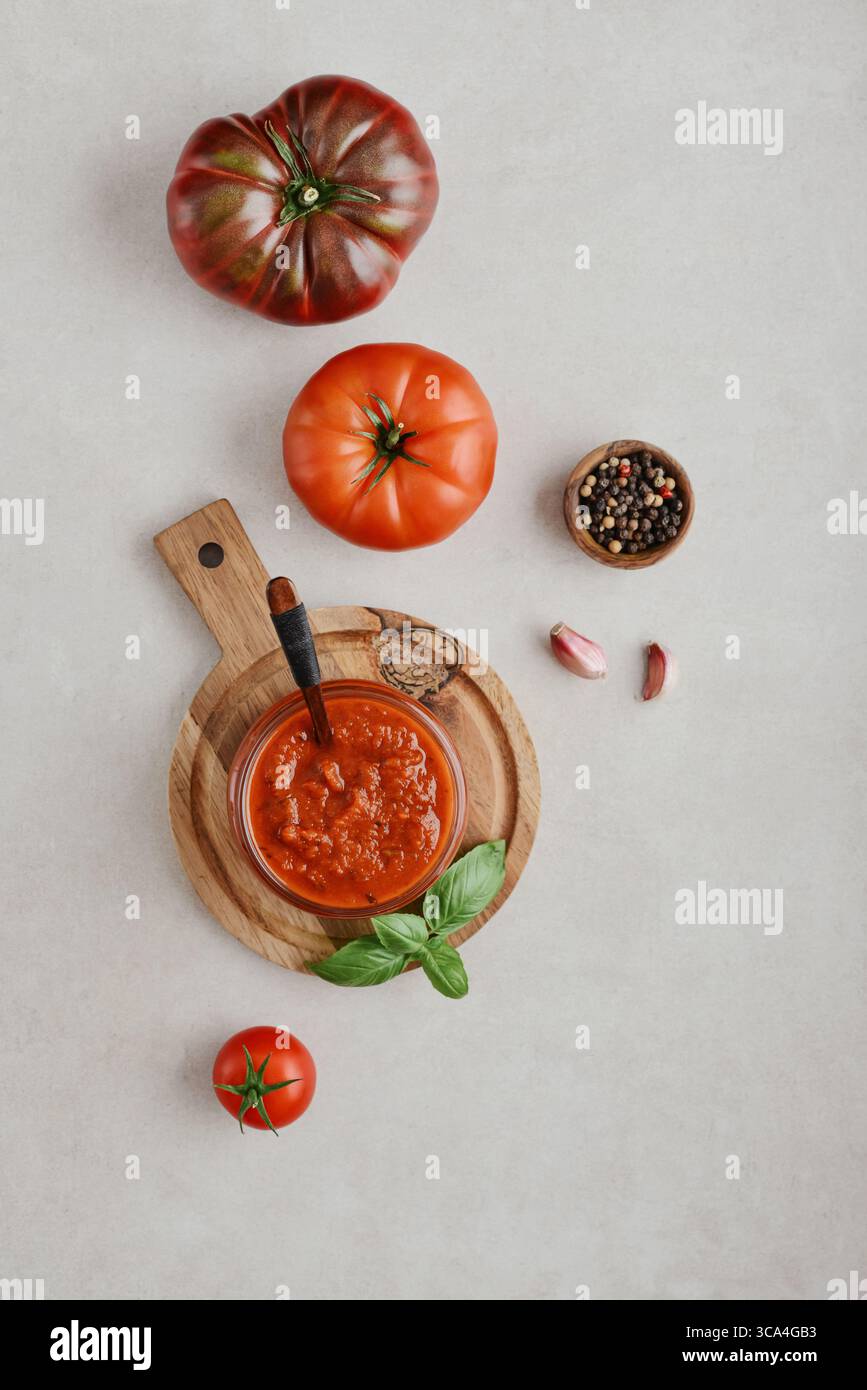 Traditional tomato sauce in a glass jar with fresh basil, ripe tomatoes, garlic and pepper on wooden cutting board, top view Stock Photo