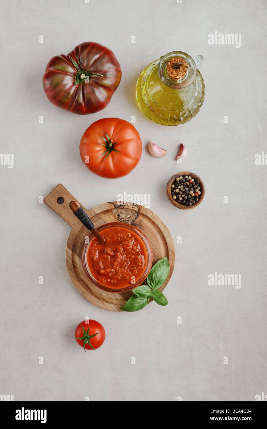 Traditional tomato sauce in a glass jar with fresh basil, ripe tomatoes, garlic and pepper on wooden cutting board, top view Stock Photo