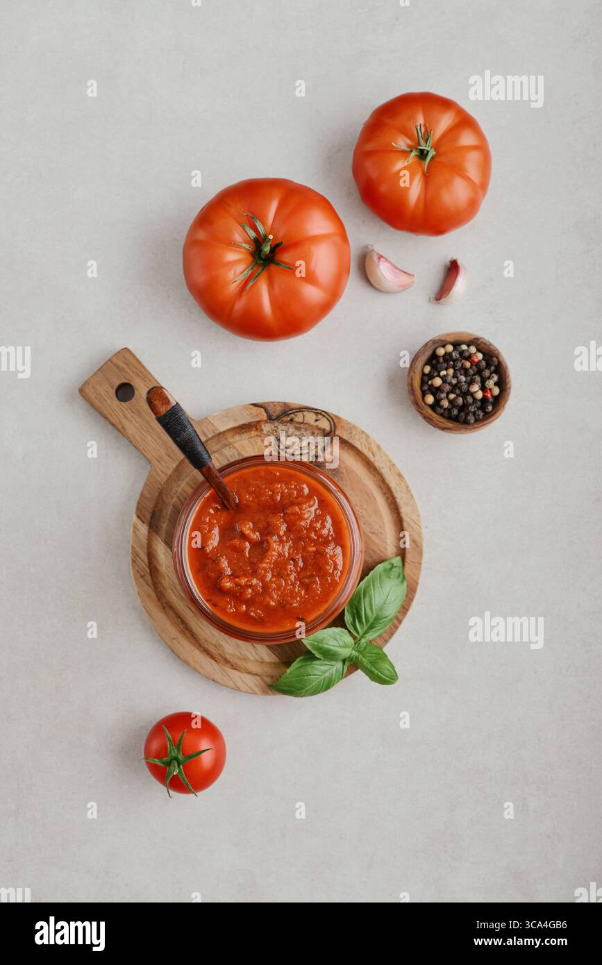 Traditional tomato sauce in a glass jar with fresh basil, ripe tomatoes, garlic and pepper on wooden cutting board, top view Stock Photo