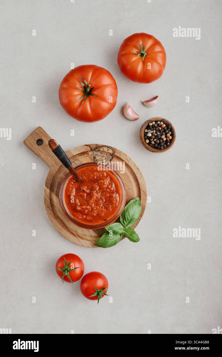 Traditional tomato sauce in a glass jar with fresh basil, ripe tomatoes, garlic and pepper on wooden cutting board, top view Stock Photo