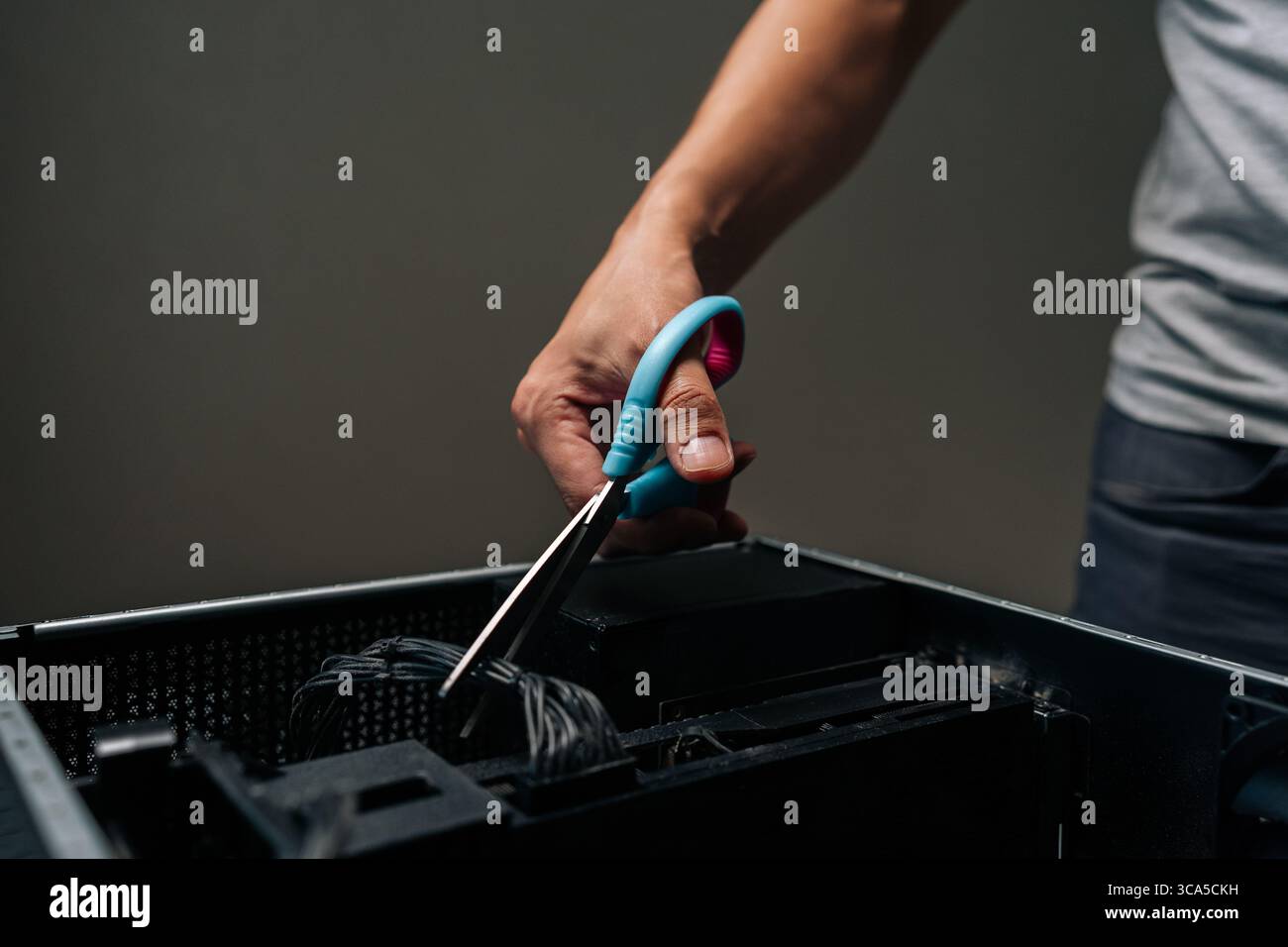 Close-up of technician hand using scissors to cut cable inside desktop computer, performing maintenance or repair work on complex internal components. Stock Photo