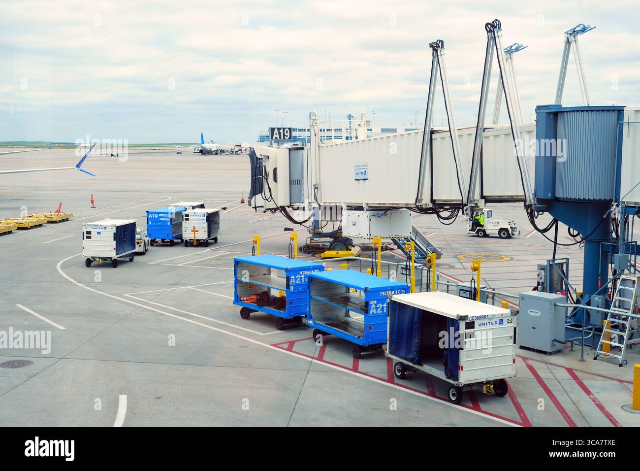 A jet bridge at the airport terminal gate with airplane, baggage vehicles and ground services. Stock Photo