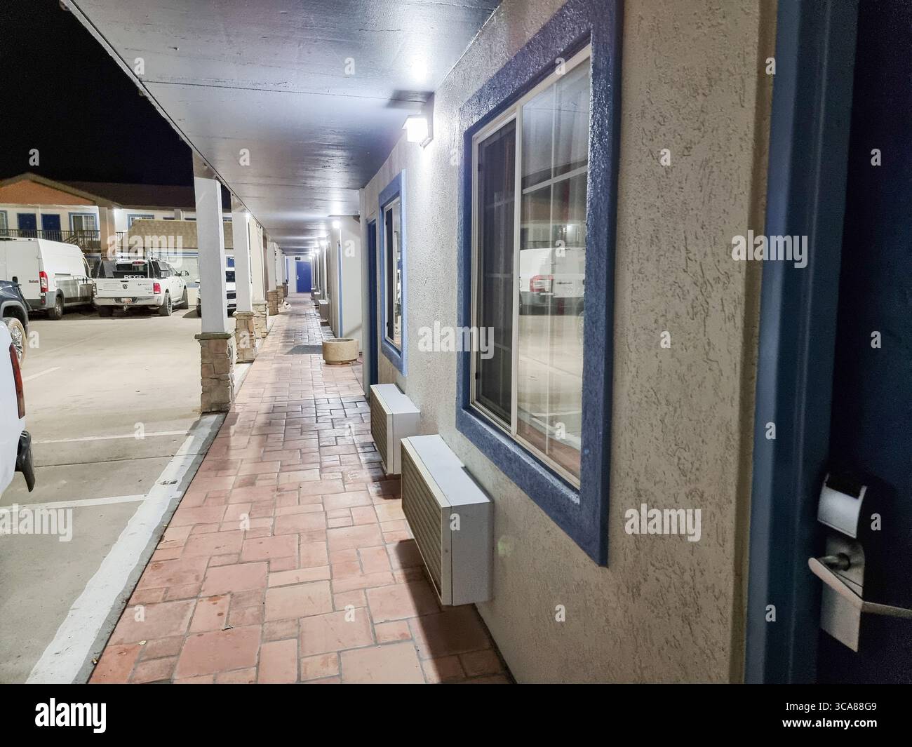 Nightly view of exterior gallery & parking of street-level hotel rooms along car parking; motel, sliding windows, key card door lock; feeling safe - Smartphone Captured Stock Image