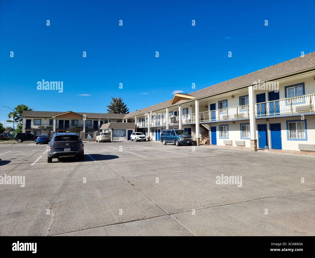 White and blue two-storey hotel with exterior galleries/corridors/doors and hotel parking under blue sky; blue hotel doors - Smartphone Captured Stock Image