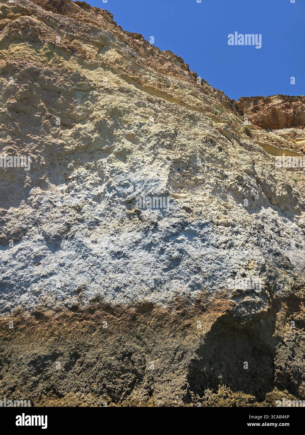 Close-up view of steep limestone sea cliffs on the Algarve coast, Portugal, showing layered rock formations and signs of coastal erosion under a clear - Smartphone Captured Stock Image