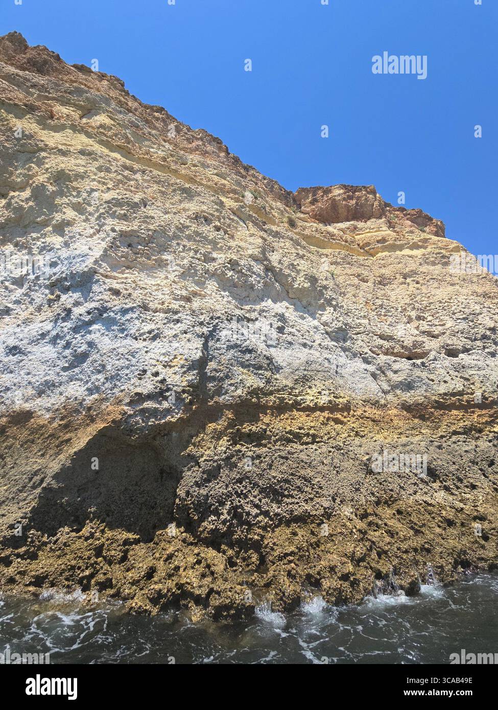 Close-up view of steep limestone sea cliffs on the Algarve coast, Portugal, showing layered rock formations and signs of coastal erosion under a clear - Smartphone Captured Stock Image