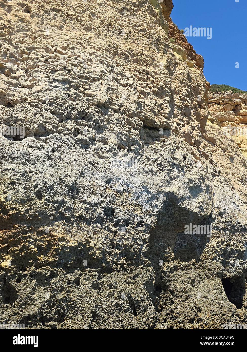 Close-up view of steep limestone sea cliffs on the Algarve coast, Portugal, showing layered rock formations and signs of coastal erosion under a clear - Smartphone Captured Stock Image