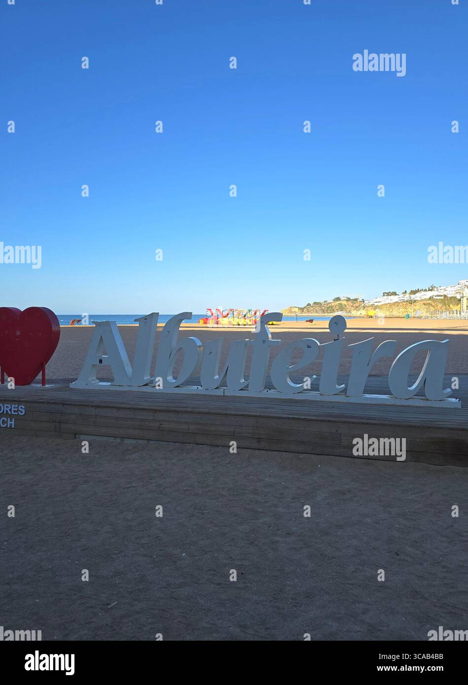 “I ❤️ Albufeira” sign on the beach promenade in Albufeira, Algarve, Portugal, with the Atlantic Ocean in the background under a clear blue sky. - Smartphone Captured Stock Image