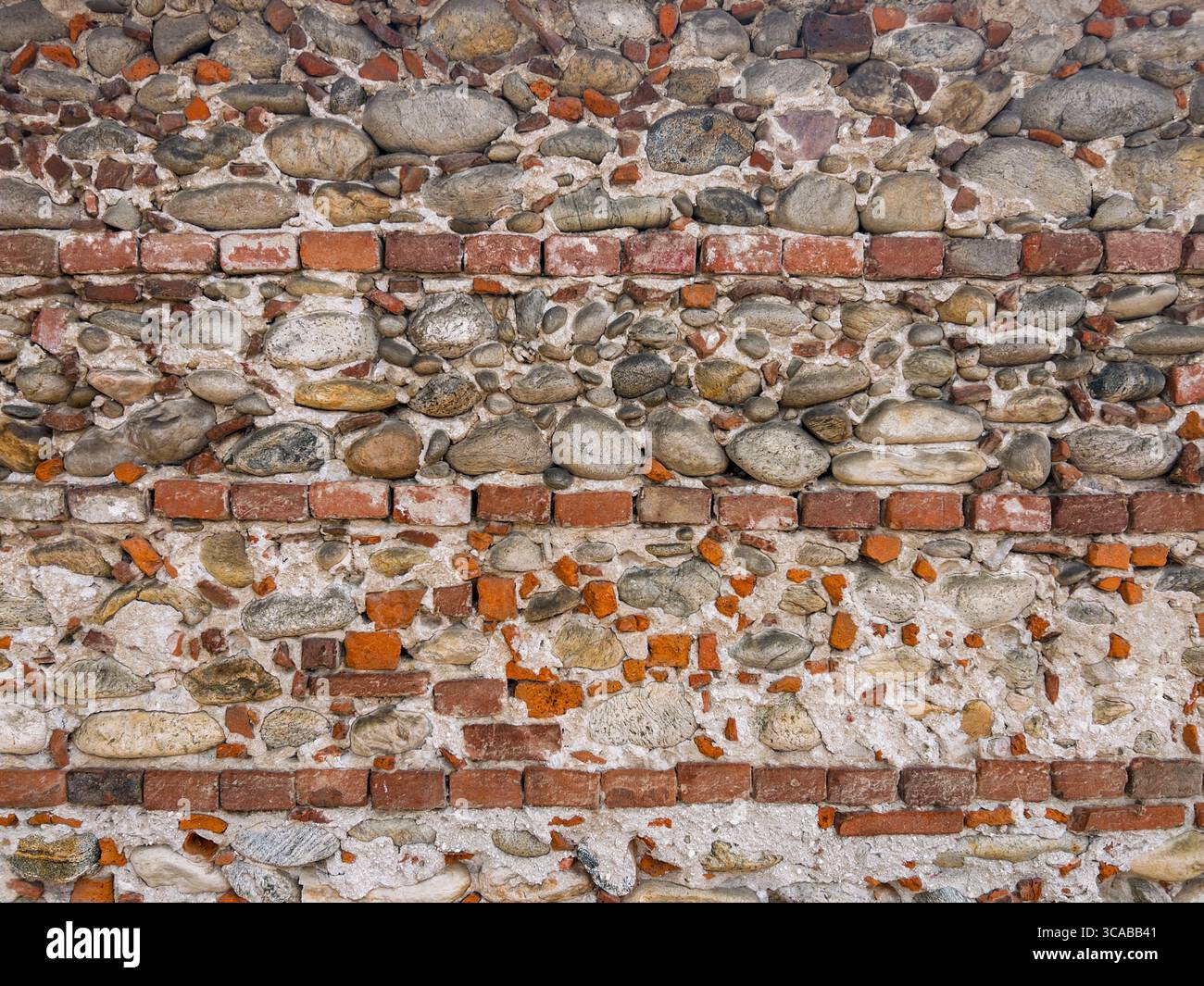 Old wall made of neat rows of old bricks mixed with natural stones, broken bricks, and plaster. Graphic element for background and texture. Stock Photo