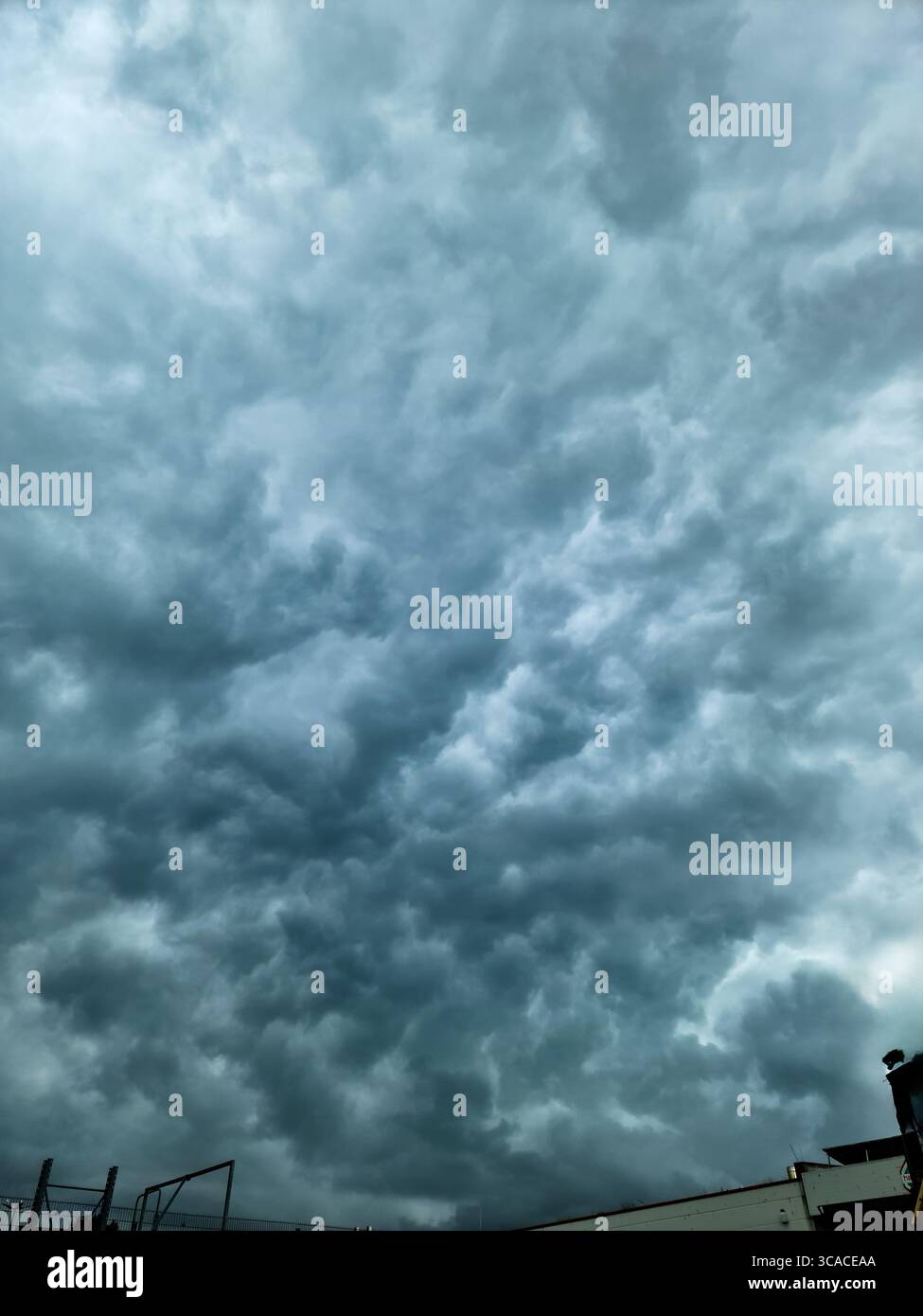 Menacing dark clouds enveloping the sky, casting a dramatic atmosphere over urban buildings and creating an ominous cityscape Stock Photo