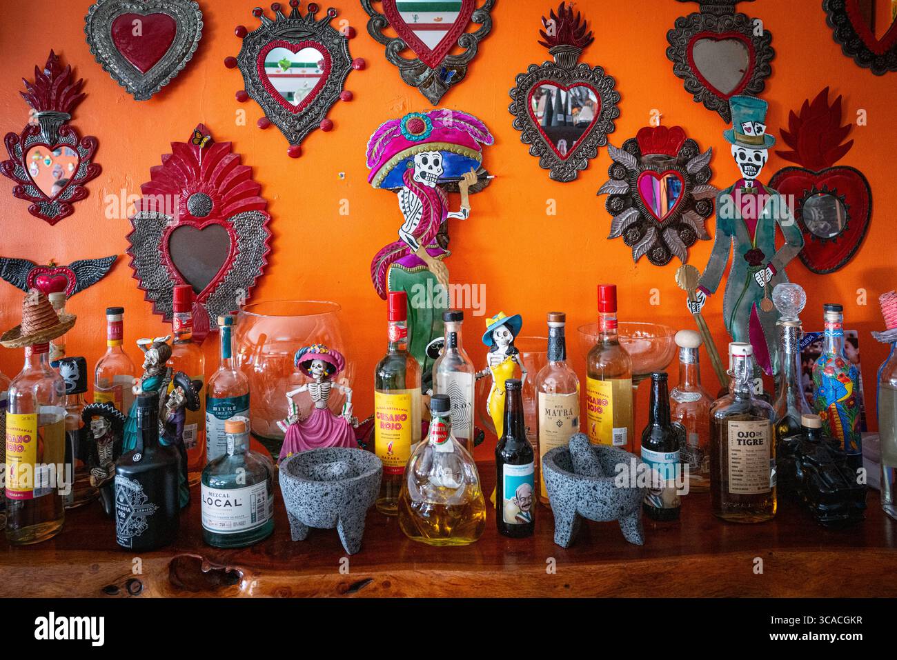 Various bottles of alcohol displayed in front of a colorful decorated orange wall in a bar area with Molcajete (mortar and pestle) in Baja, California Stock Photo
