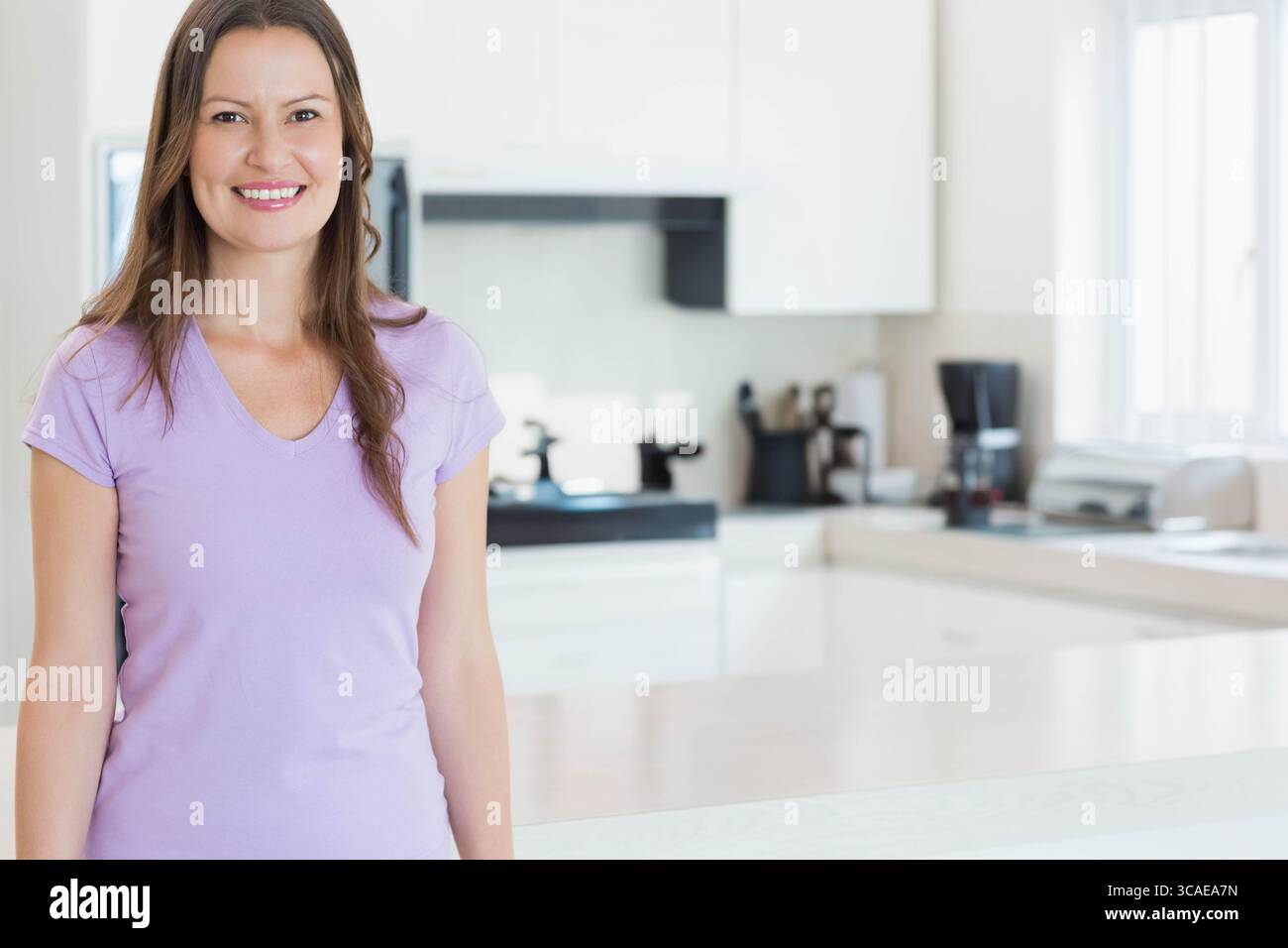 Woman wearing lavender shirt standing beside kitchen island with microwave in kitchen, copy space Stock Photo