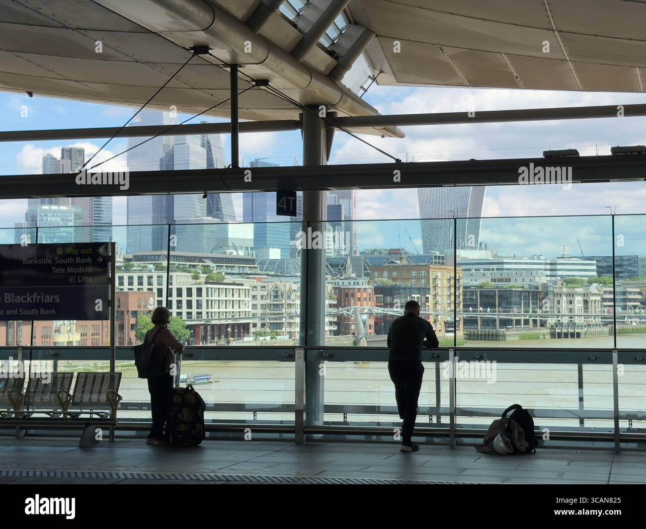 Two commuters stand on the platform at Blackfriars station, London, looking out onto the river Thames and the London skyline. Silhouettes. - Smartphone Captured Stock Image