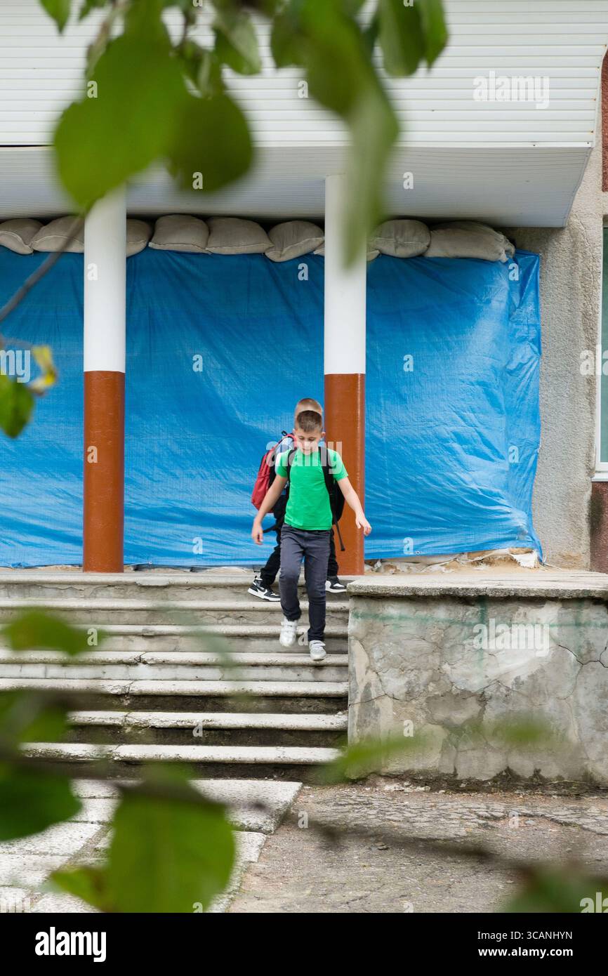 Two school children with backpacks are walking down the steps of a building. The building is covered with a blue tarp and sandbags. The setting convey Stock Photo