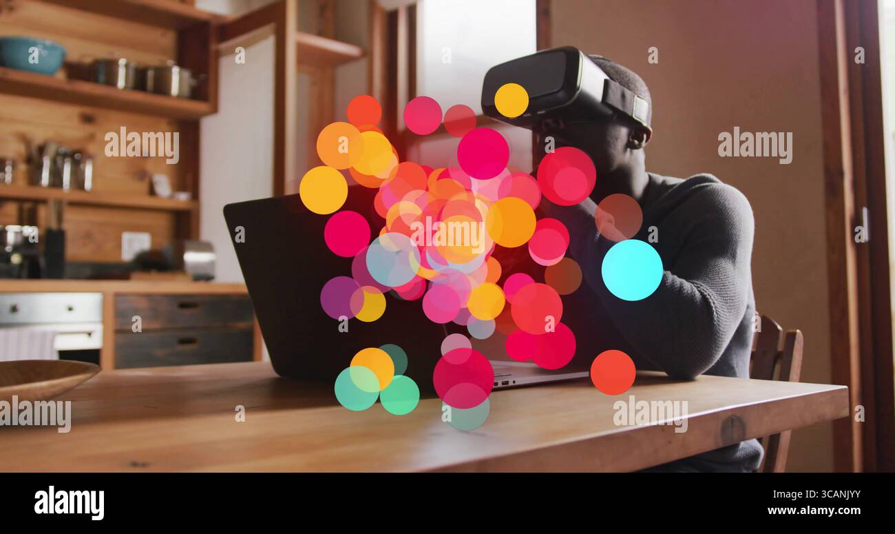 Exploring virtual space man wearing VR headset using laptop in kitchen, with colorful bokeh Stock Photo