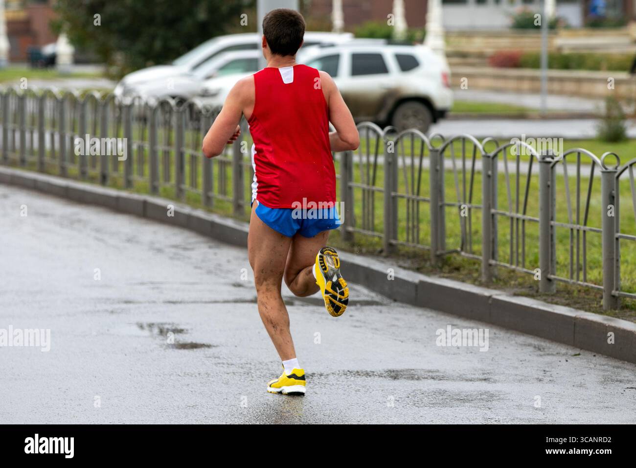 rear view runner running marathon on wet road, splashing mud on his ...