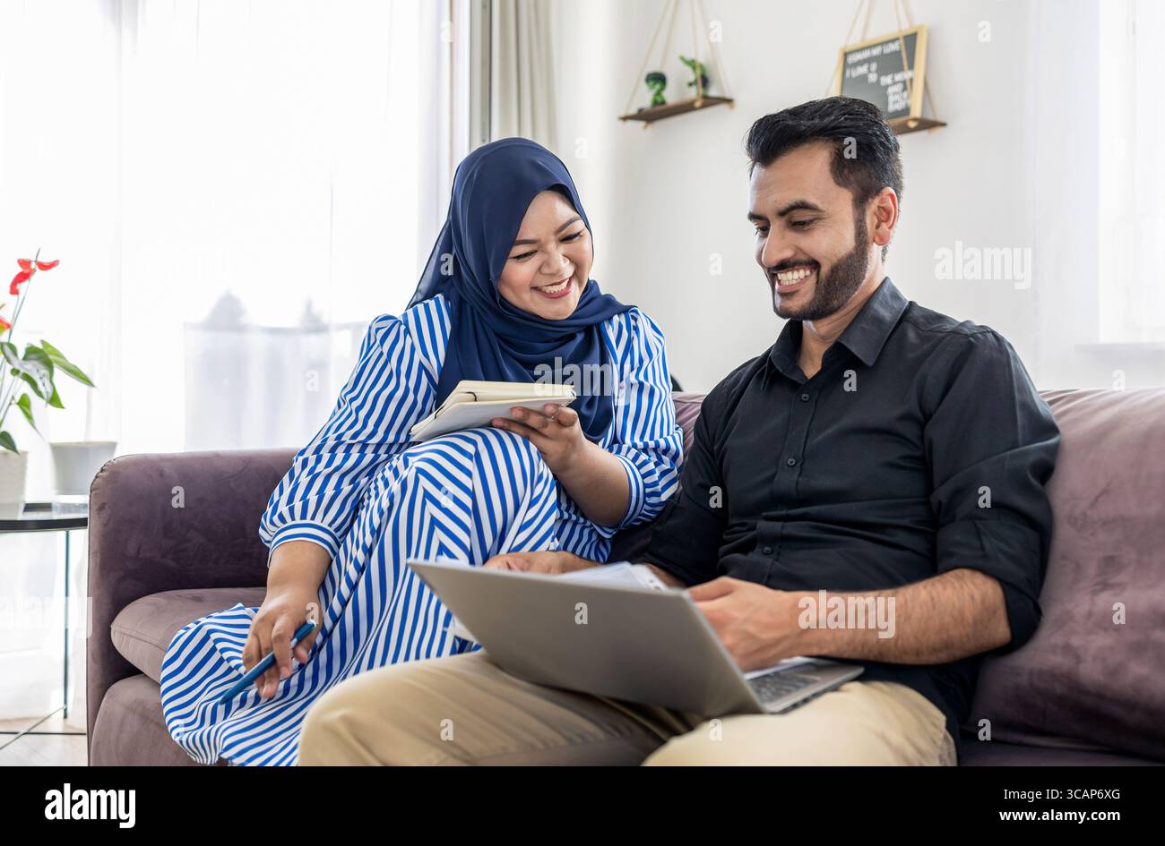 Muslim Couple using laptop Together on Sofa at Home Stock Photo