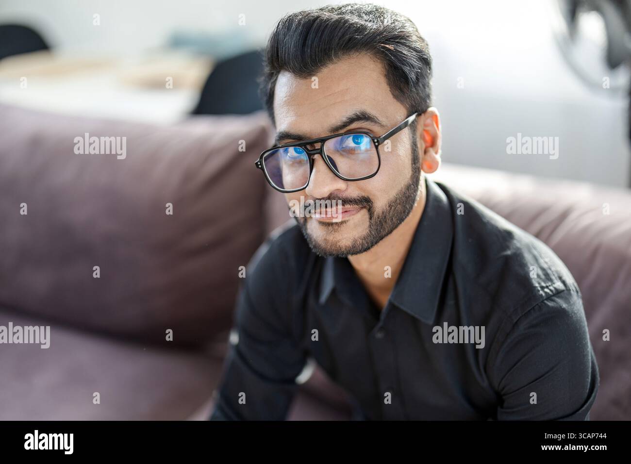 Bearded man sitting on a sofa in the living room of his home and looking at camera Stock Photo