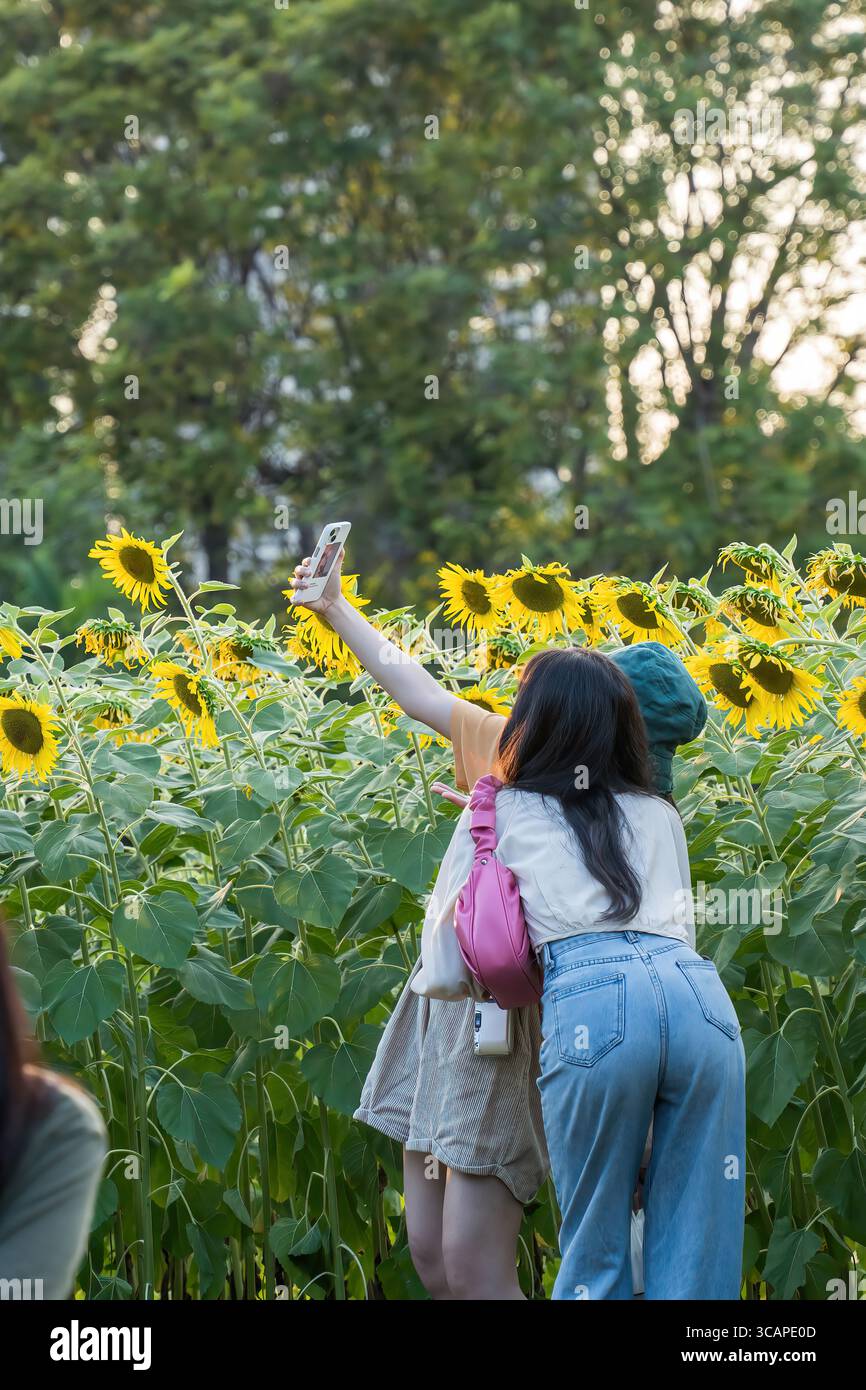 Two girls pose closely for a selfie in front of a tall blooming ...