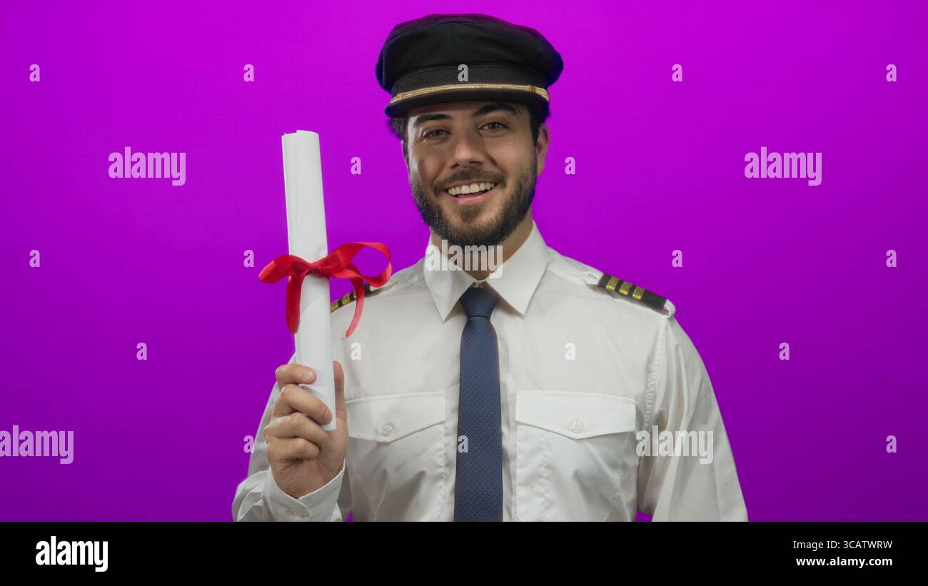 Young man in pilot uniform holding diploma against bright pink backdrop ...
