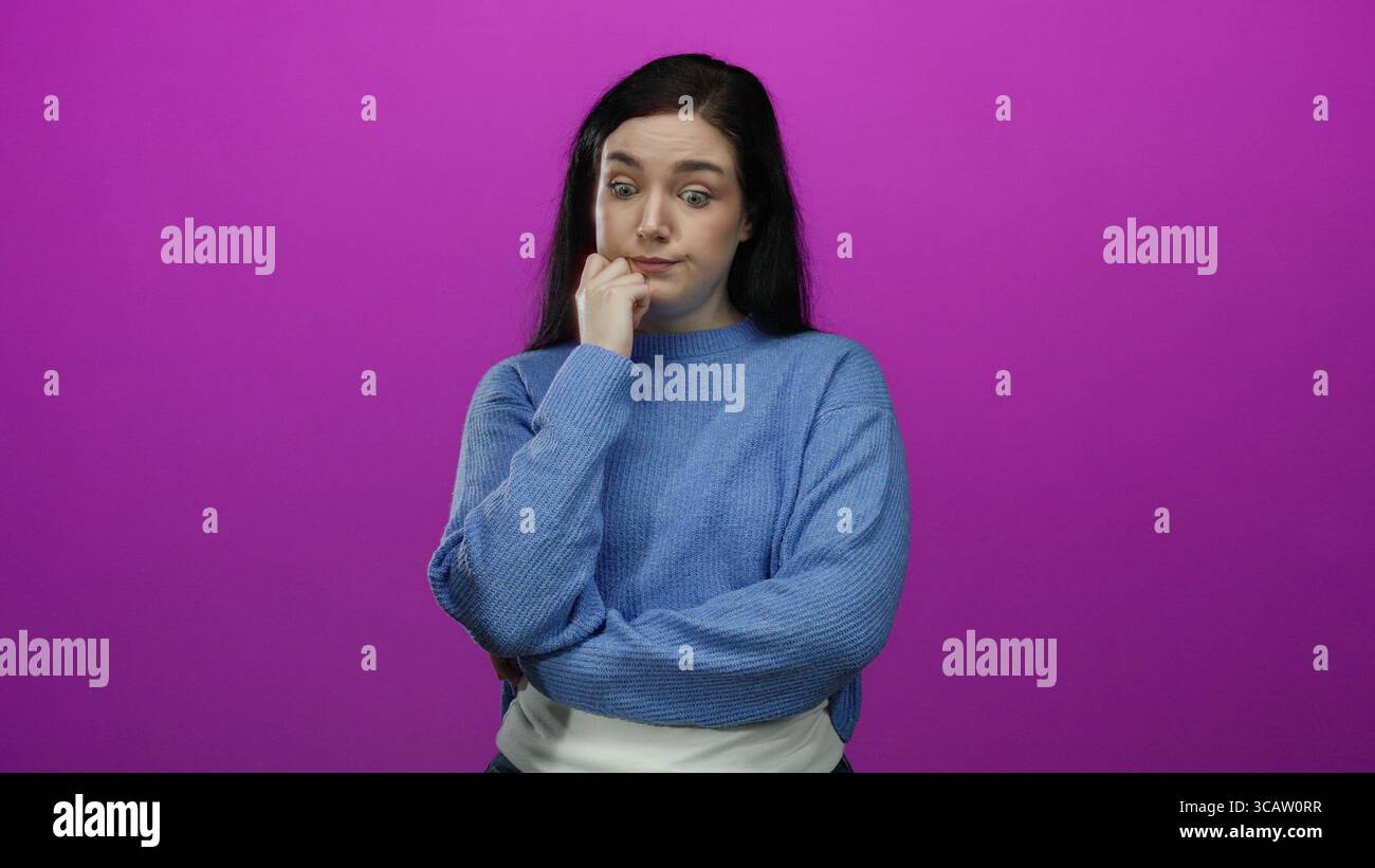 Woman standing against a vibrant pink background, wearing a blue sweater, with brunette hair, expressing contemplation with crossed arms and thoughtfu Stock Photo