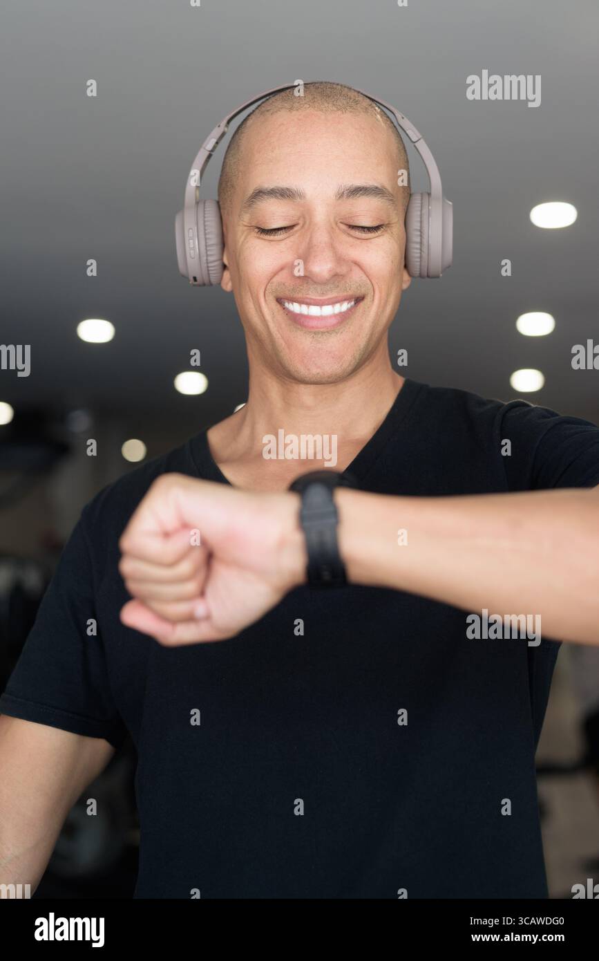 Hispanic bald man athlete in gym using smartwatch fitness tracker monitoring his exercise stats and heart rate with wearable technology in modern gym Stock Photo