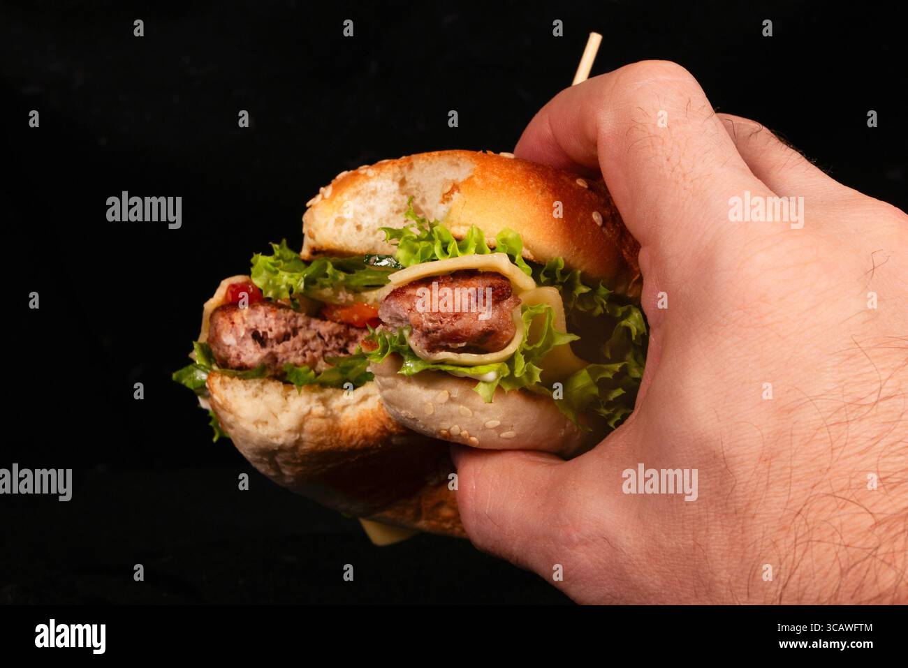 Hand holding a bitten burger with melted cheese, lettuce, tomato ...