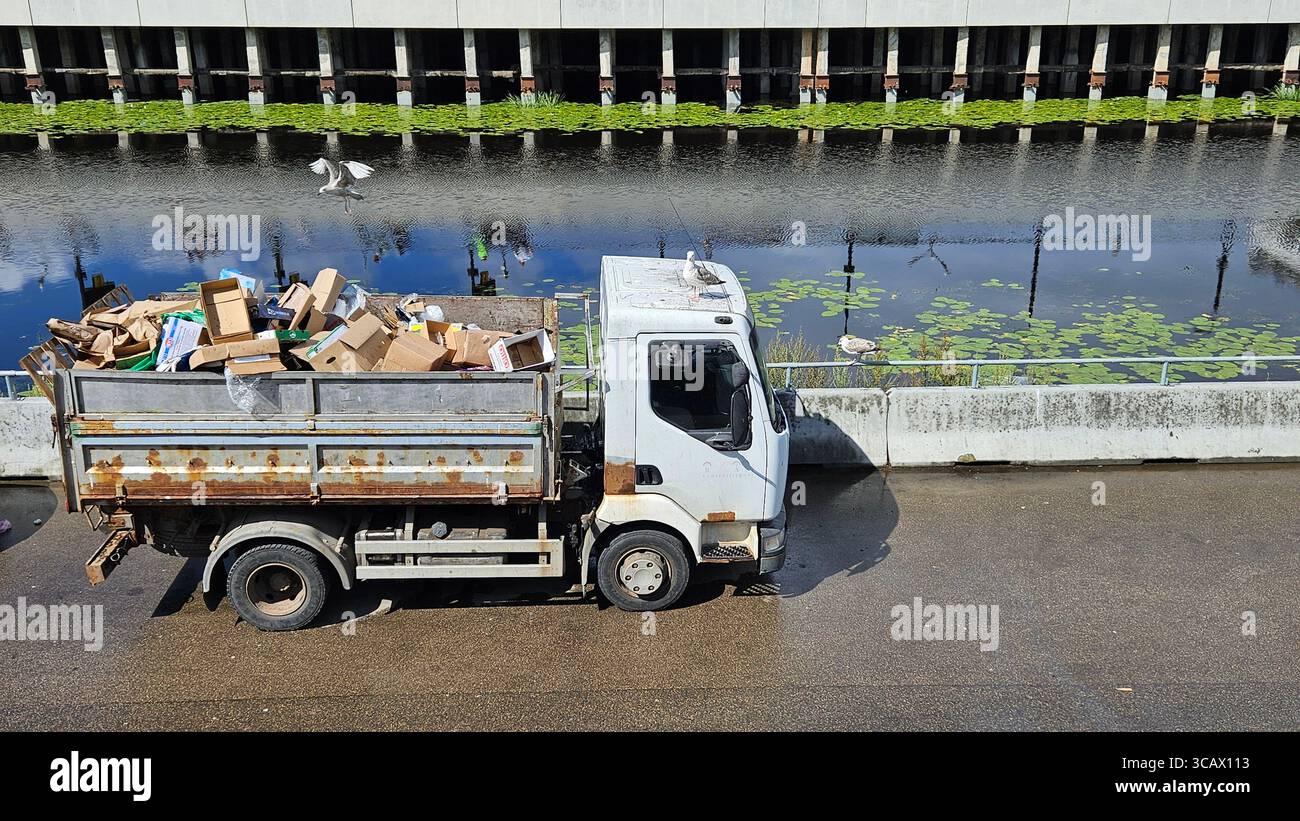 Rusty Garbage Truck by Canal with Seagulls and Cardboard Waste.Urban waste management and recycling concept. - Smartphone Captured Stock Image