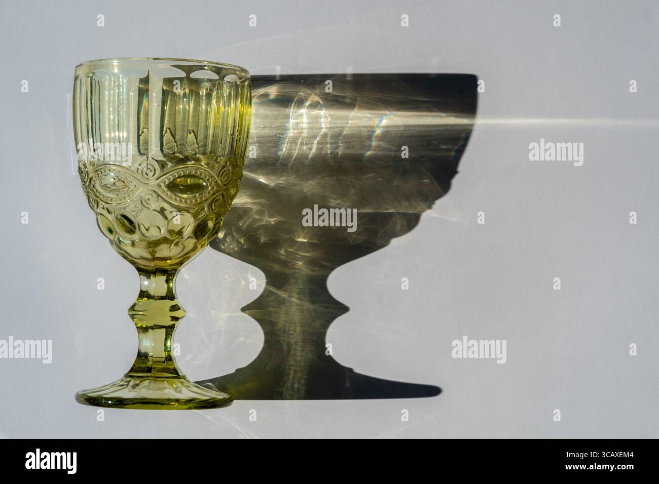 Green glass goblet with water. Abstract shadow pattern on white background Stock Photo