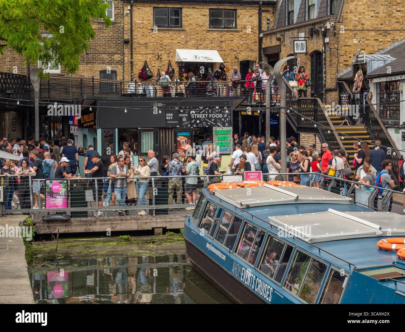 A London Waterbus docks beside the bustling street food stalls of Camden Market on the Regent's Canal in London, UK. Stock Photo