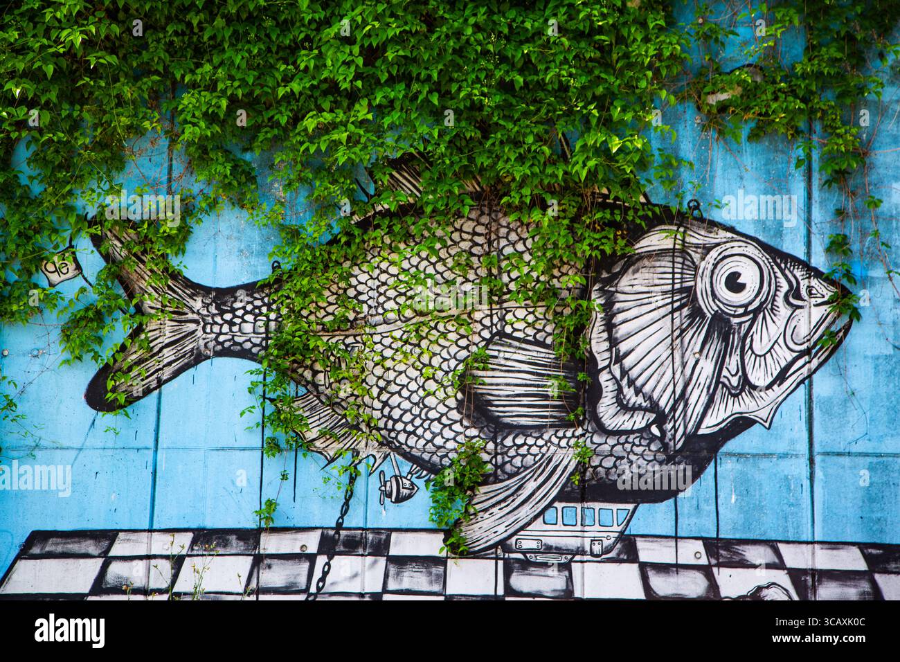 Detailed fish mural blending naturally with vibrant green foliage urban ...