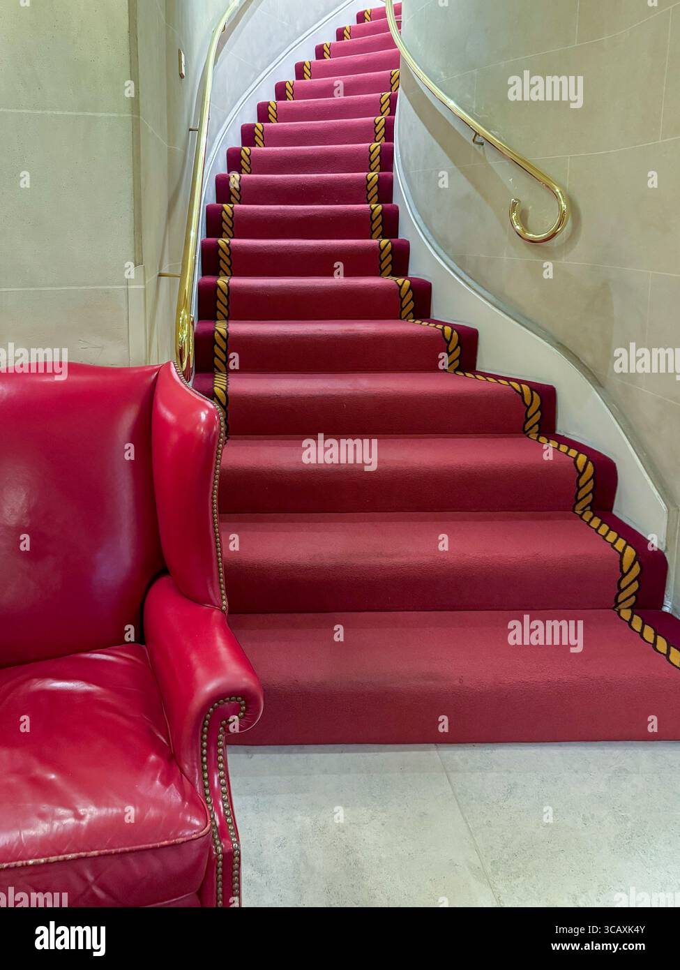 An elegant curved staircase with a luxurious deep red carpet, inside the world-famous Ritz hotel in Mayfair, London, UK. Stock Photo