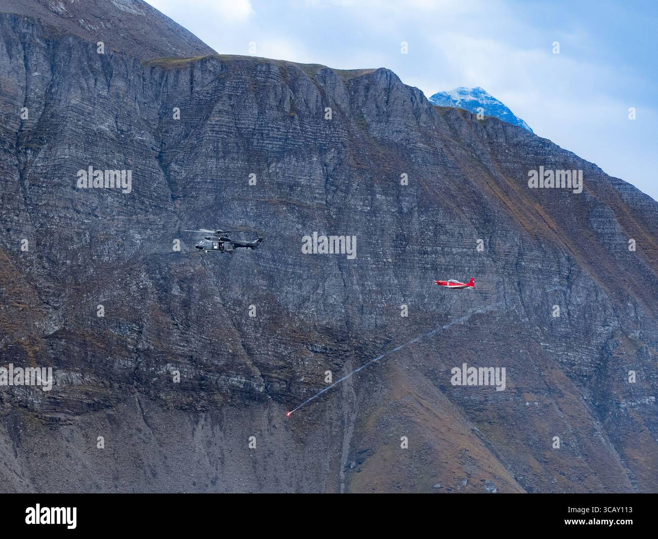 Swiss Military Helicopter and Trainer Aircraft Flying in the Alps with Flare During Airshow Stock Photo
