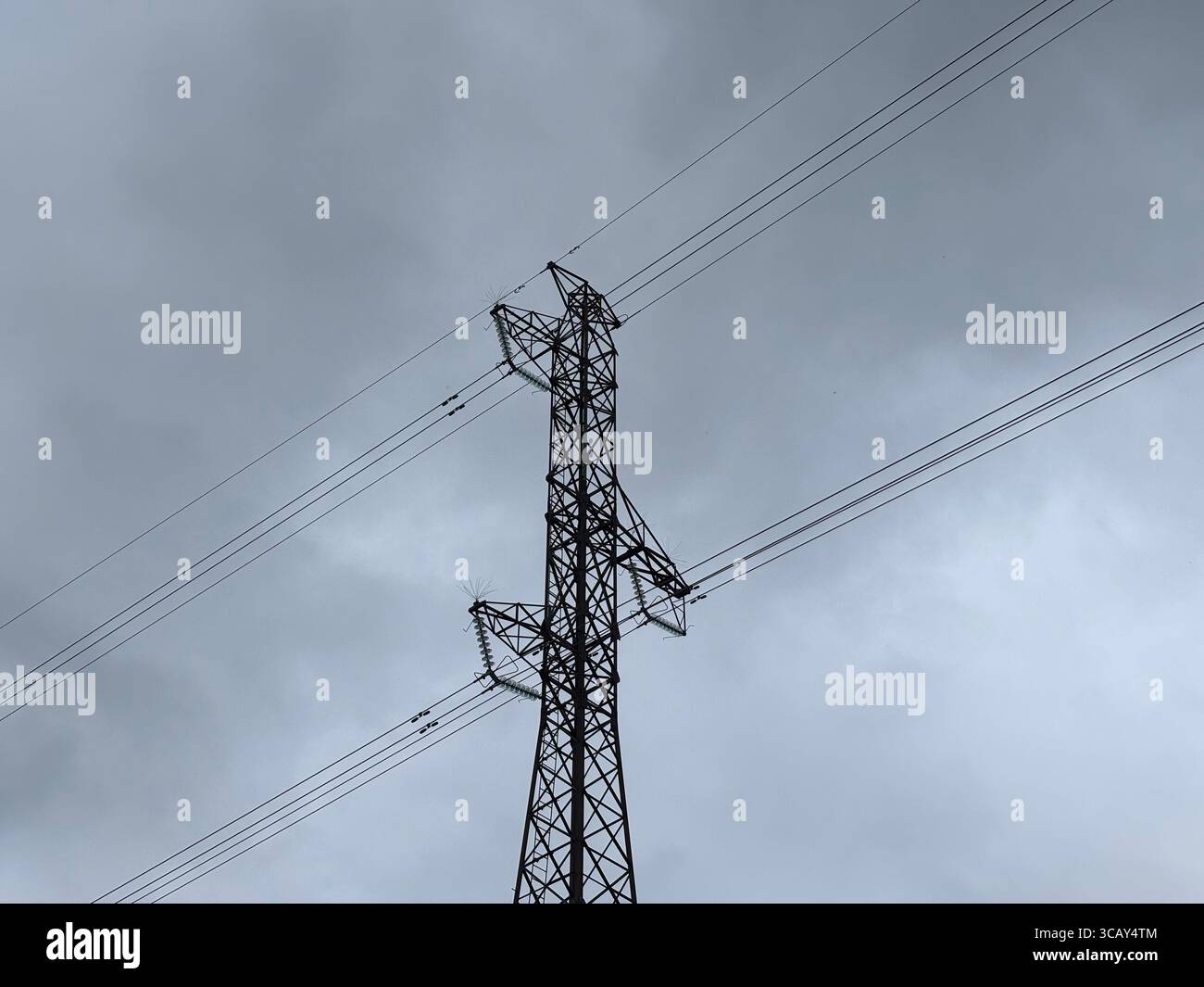 Electricity cables and electricity pylons against a grey cloudy sky. - Smartphone Captured Stock Image